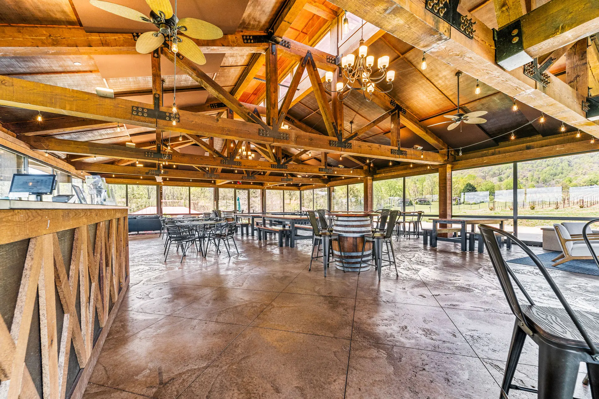 Winery tasting room with wooden beams, metal chairs, and vineyard views.