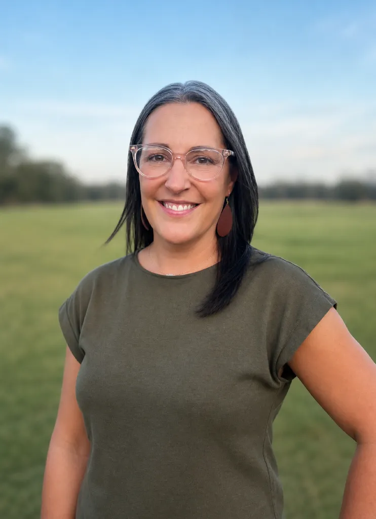 Smiling woman with glasses and gray hair wearing a green top outdoors in a field.