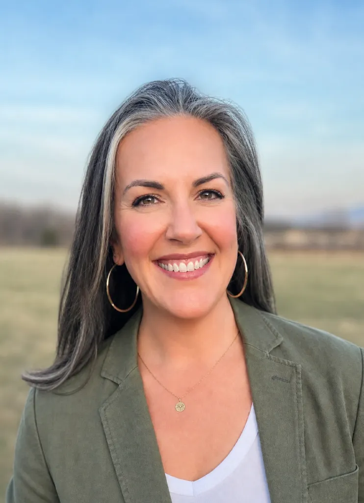 Smiling woman with gray hair wearing hoop earrings and a green blazer outdoors.