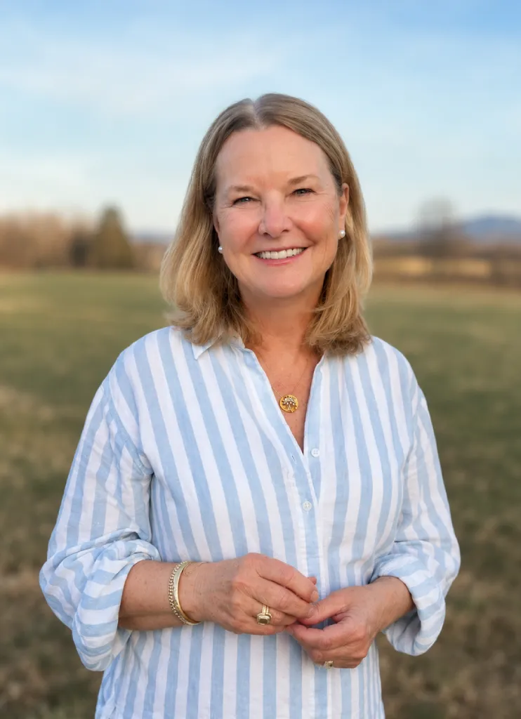 Smiling woman standing outdoors in an open field wearing a blue and white striped blouse during golden hour.