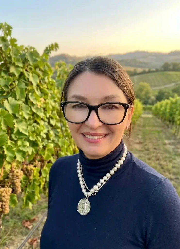 Woman smiling in a vineyard with rolling hills in the background.